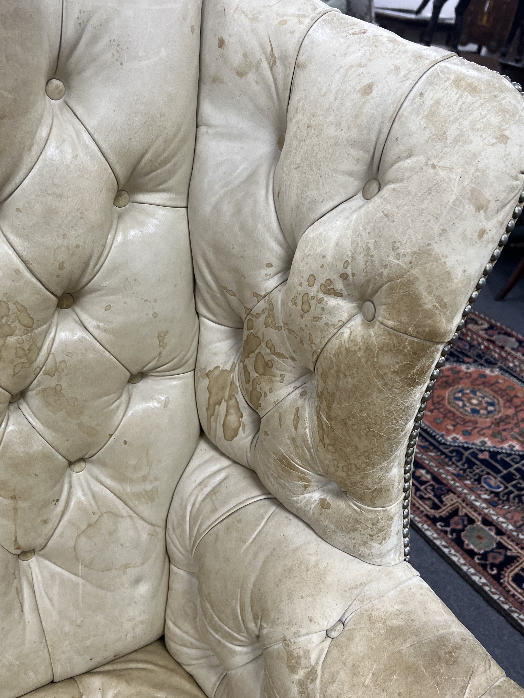 A George III style mahogany and buttoned leather wing armchair, width 80cm, depth 75cm, height 110cm with footstool